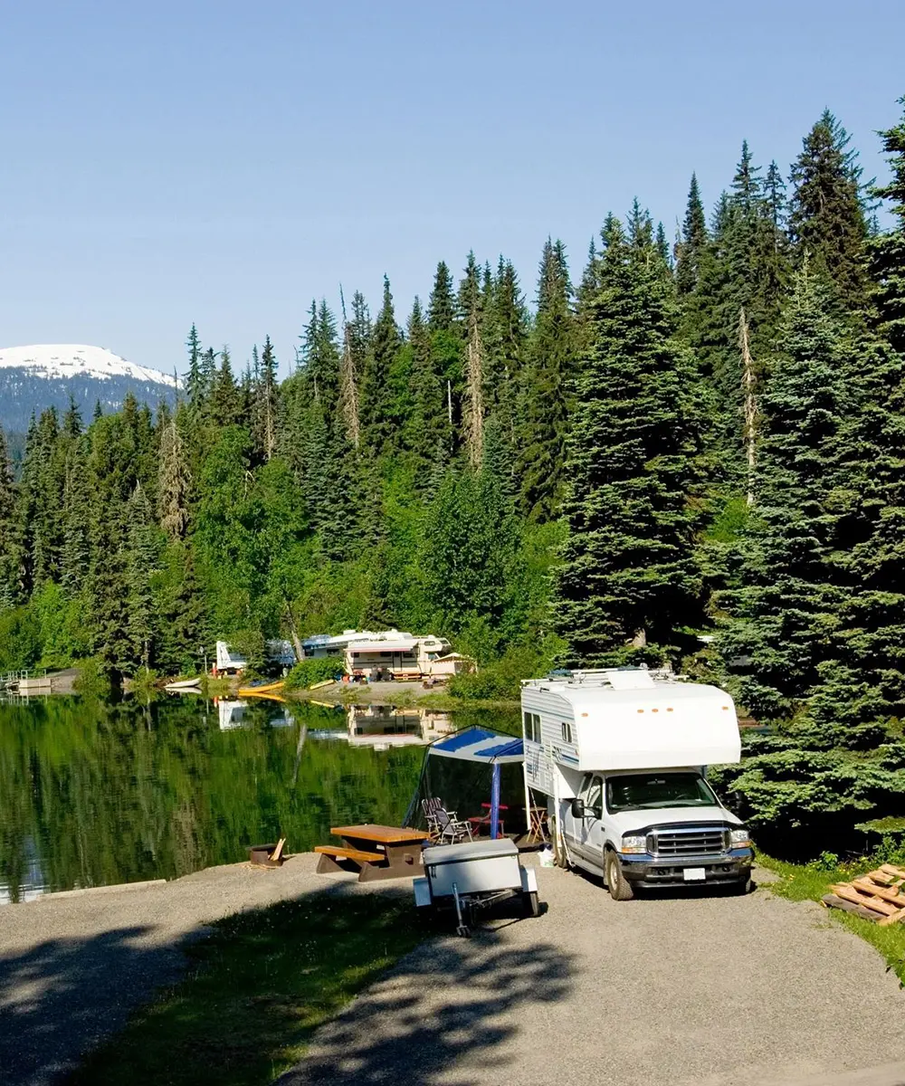 01a A camper van parked near a lake surrounded by tall pine trees.