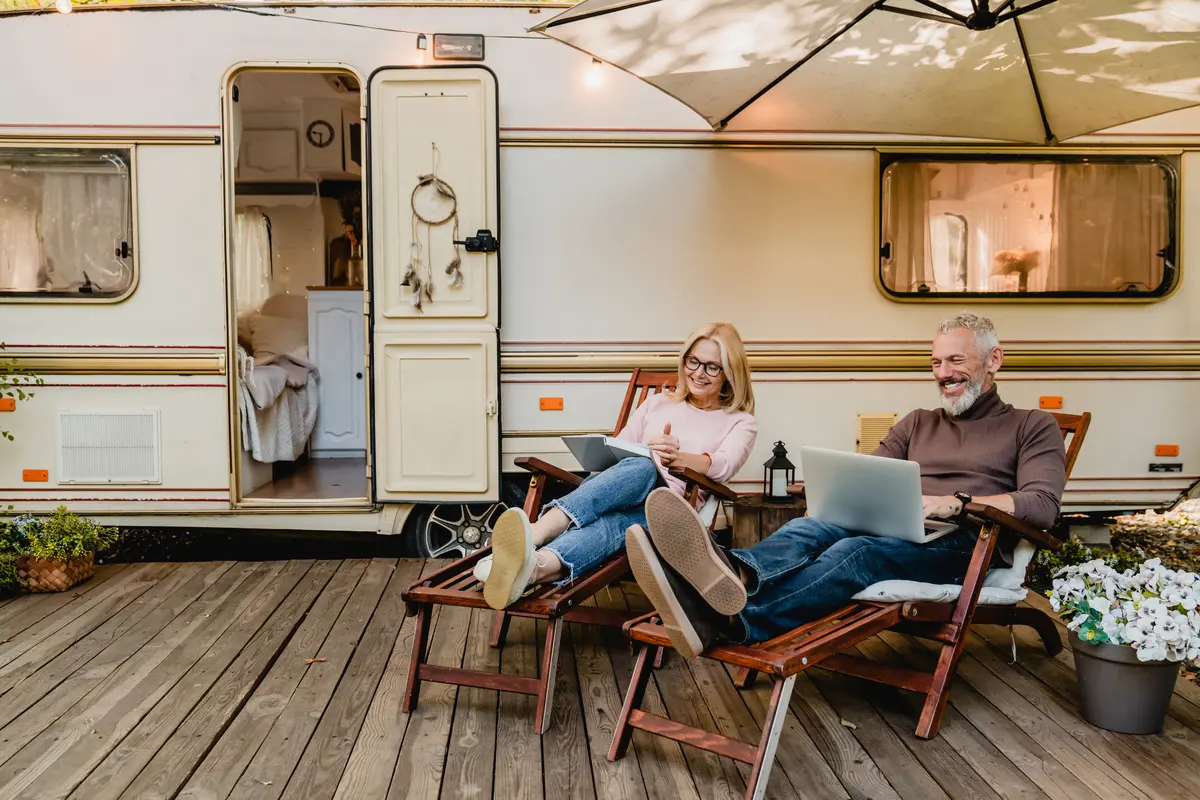 Couple relaxing outside camper with laptops.