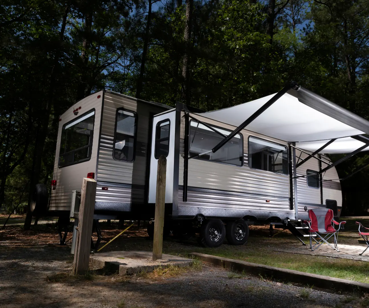 GettyImages-2017828436 Camper trailer with awning in wooded area.