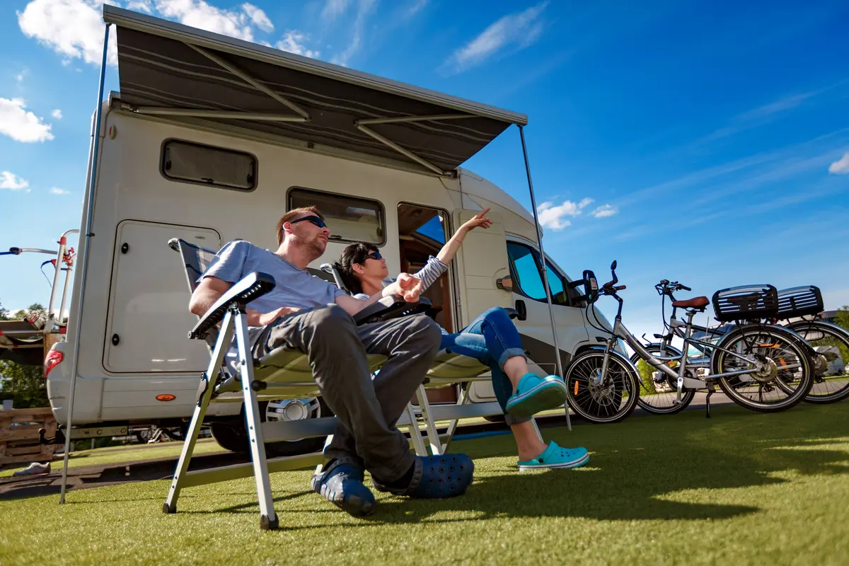 Couple relaxing by camper with bicycles nearby.